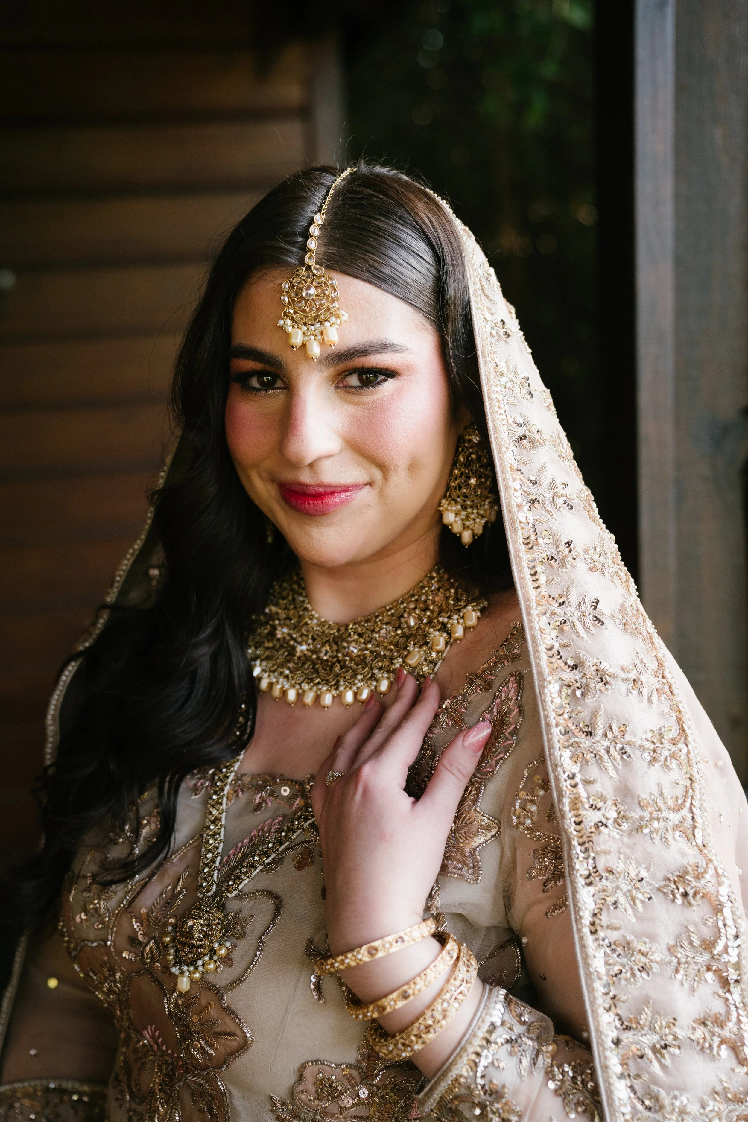 A woman wearing traditional Indian bridal attire with elaborate gold jewelry and an embroidered dupatta.