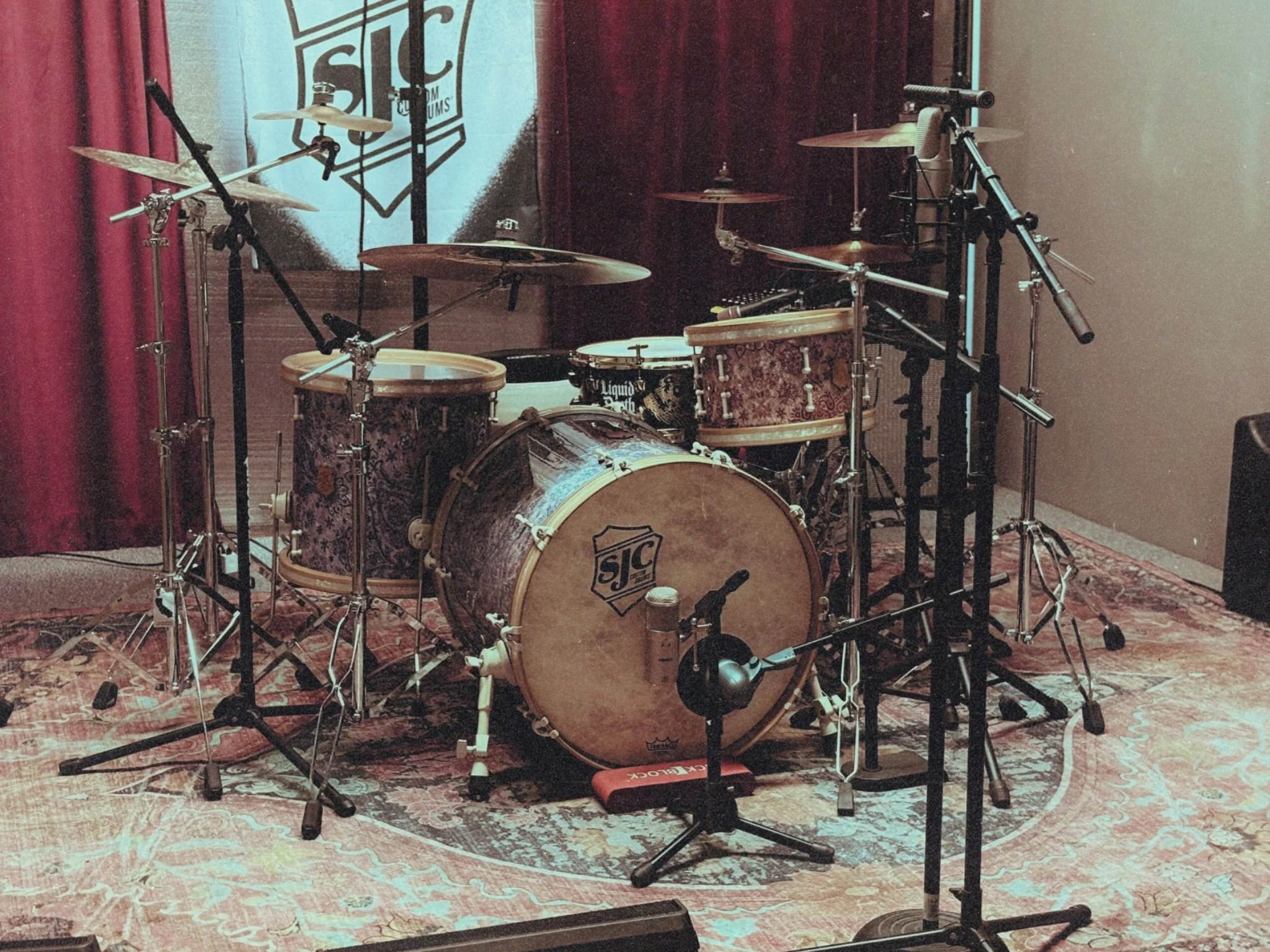 A drum set on a stage with microphones and stands in front of a backdrop with the SIC logo.