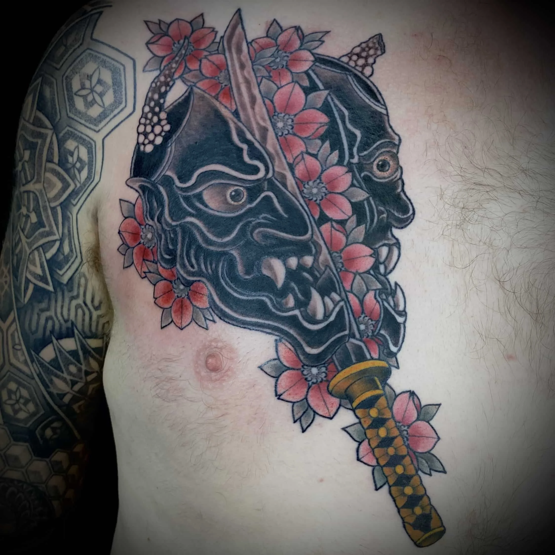 Japanese Hannya mask tattoo depicting a samurai sword slicing the mask in half.  Spilling out are colorful sakura cherry blossoms.  Created by Cohen Floch at his tattoo shop in Victoria, BC.