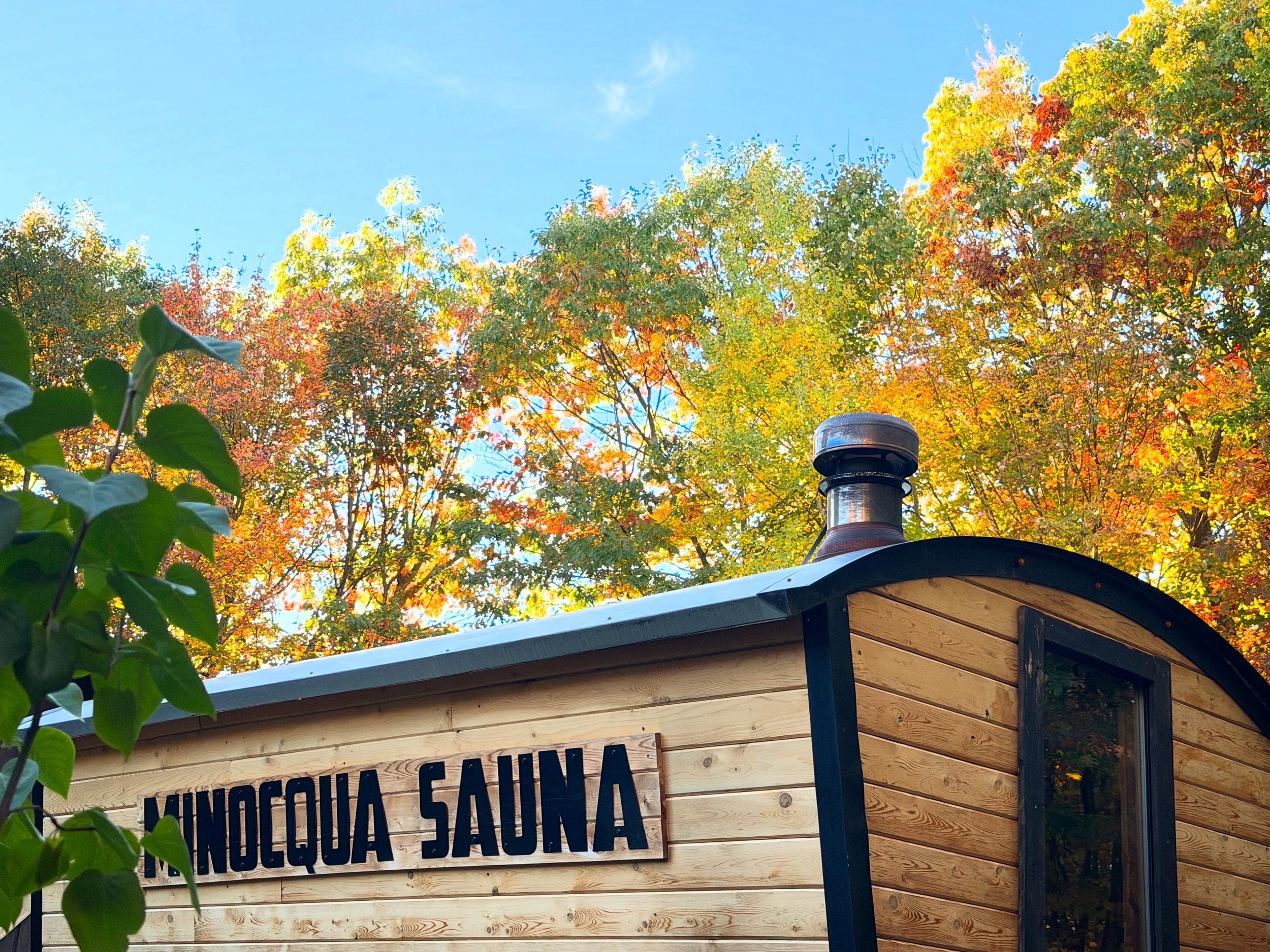 Minocqua Sauna Mobile sauna unit parked in front of fall foliage during peak color change season. Sunny Autumn day with Minocqua Sauna prominently displayed