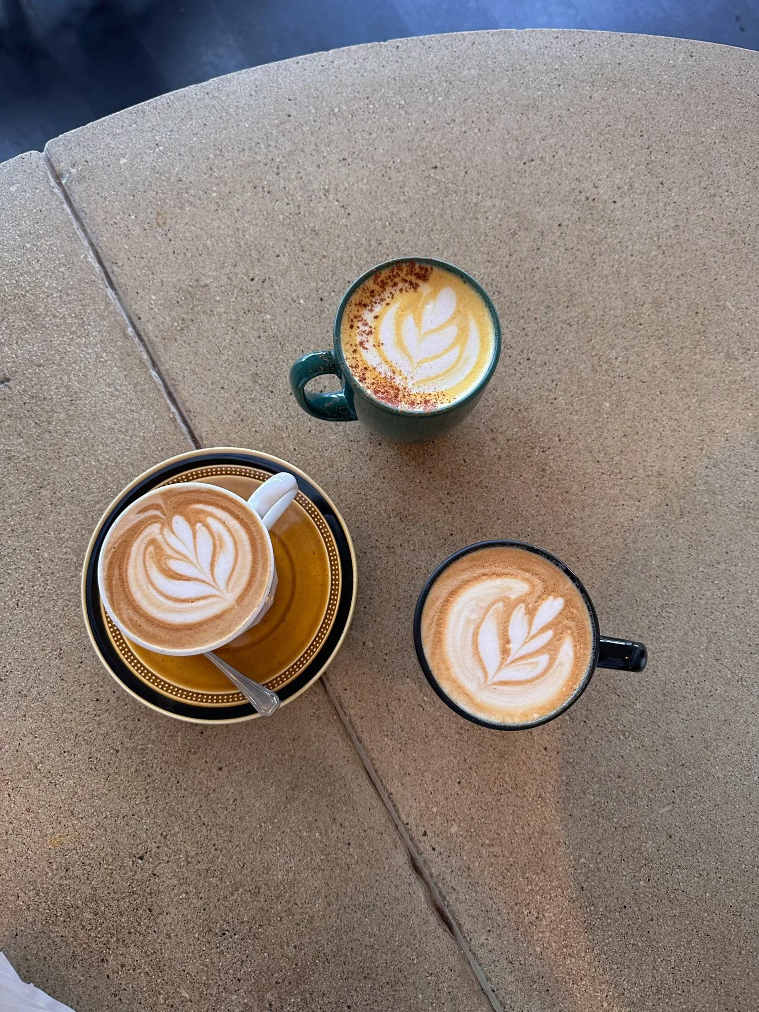 Three cups of latte art coffee on a concrete patio table
