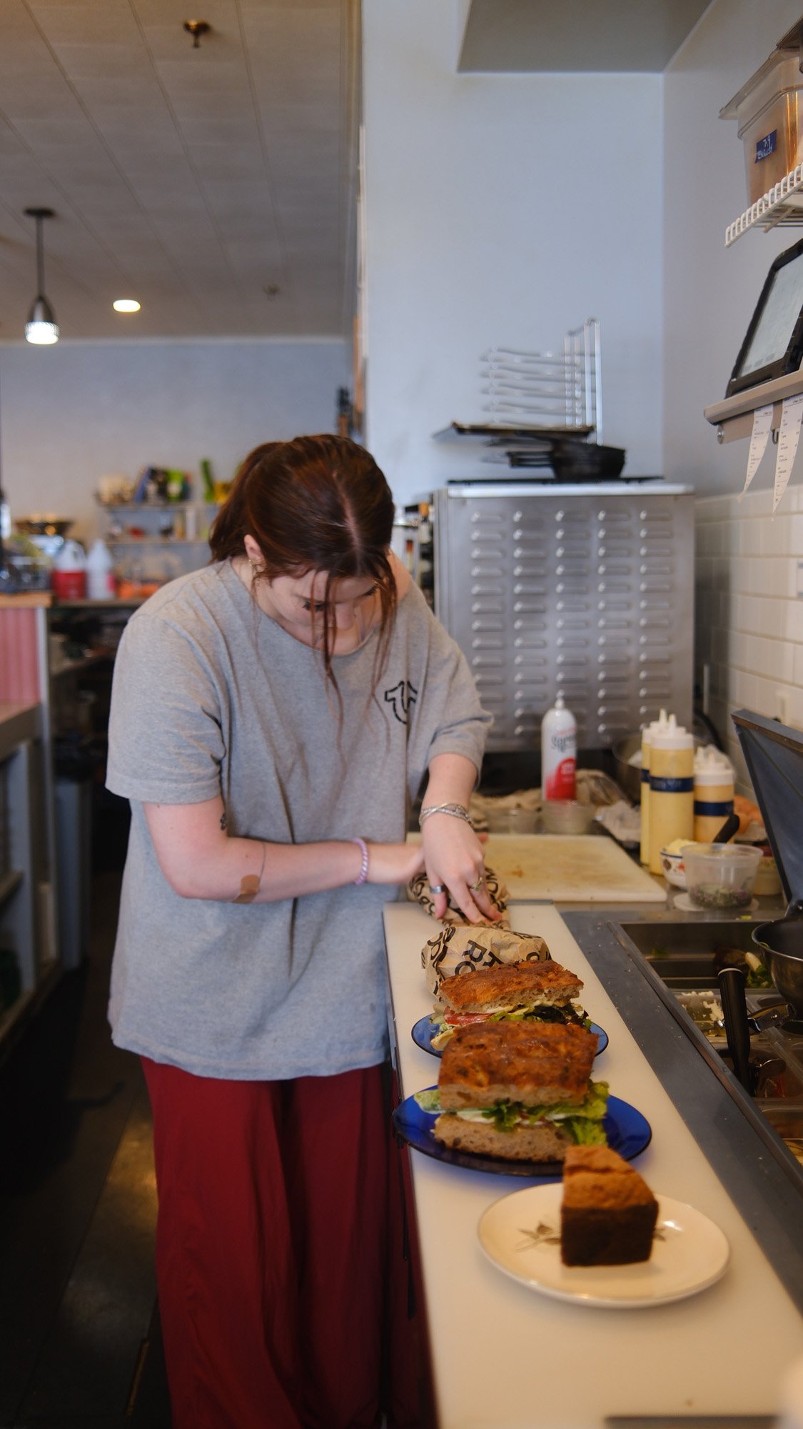 Food worker preparing sandwiches and sliced cake at a deli counter