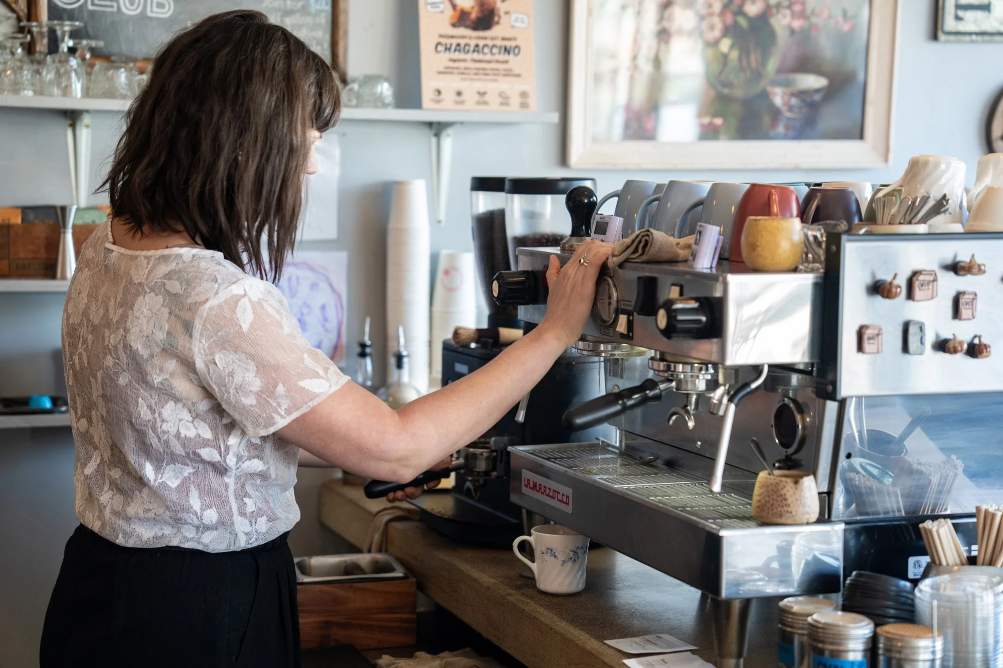 Barista operating a commercial espresso machine in a cozy coffee shop