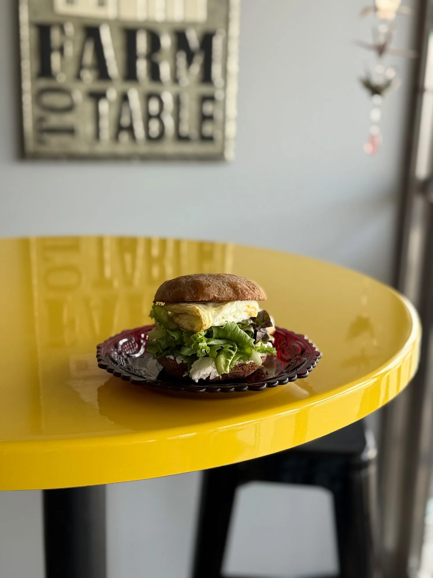 Gourmet fried egg and lettuce sandwich on a black plate atop a yellow table