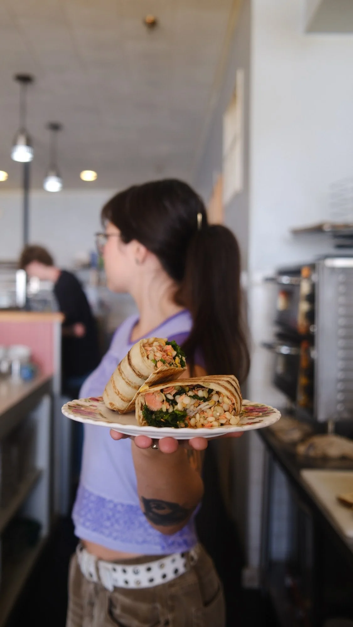 Woman holding a plate of sliced vegetable and grain wraps in a cafe