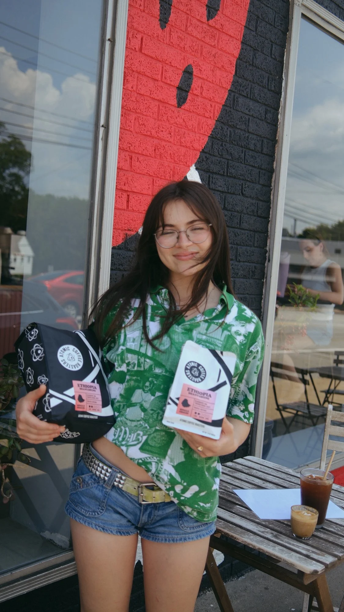 Woman wearing glasses holds two bags of Ethiopian coffee outside a café.