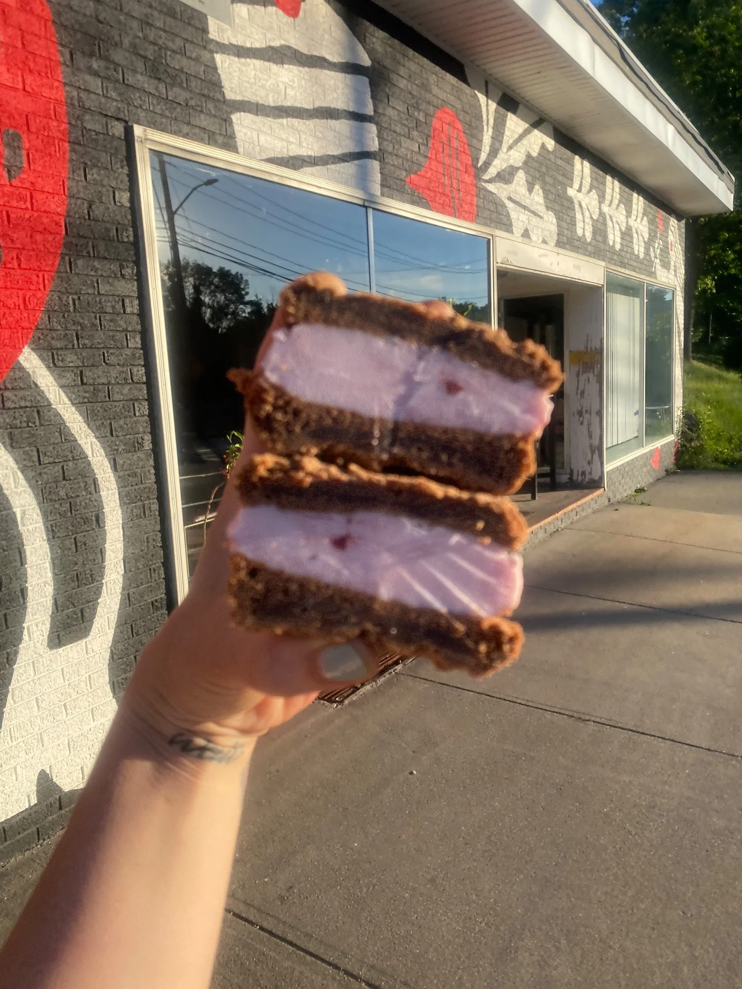 Hand holding a stack of pink-frosted brownies outside a storefront