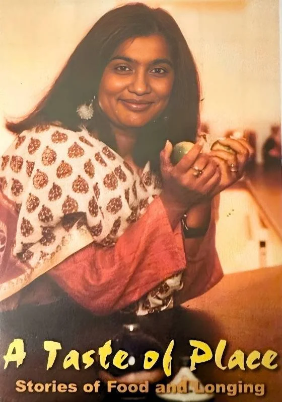 Poster for TV documentary 'A Taste of Place'. Shuchi Kothari with shoulder-length black hair, wearing traditional Indian attire with a white and gold patterned shawl and pinkish-red sleeves, holding a small green fruit, in an indoor setting.