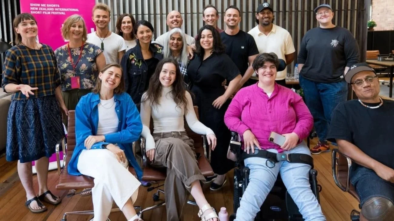 the 2025 Show Me Shorts participants pose as a group, a pink Show Me Shorts pull-up banner in the background. Shuchi Kothari is at the center of the group.