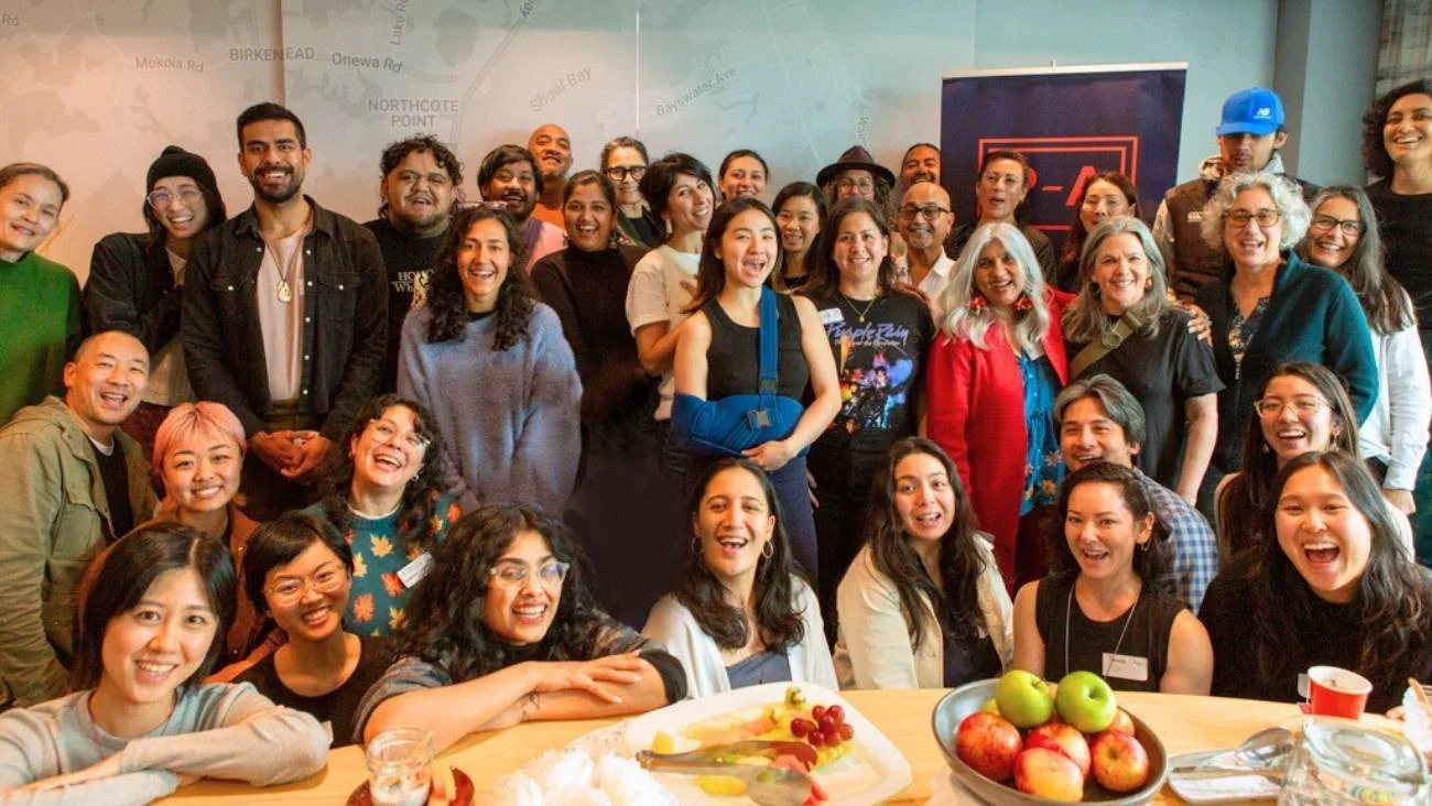 PASC participants pose for a photo indoors, smiling, with a table of fruits in the foreground.