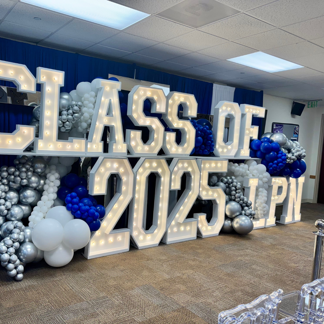 Decorative display with illuminated letters spelling Lassen 2025, surrounded by balloons in white, silver, and blue, for a 2025 graduation celebration.