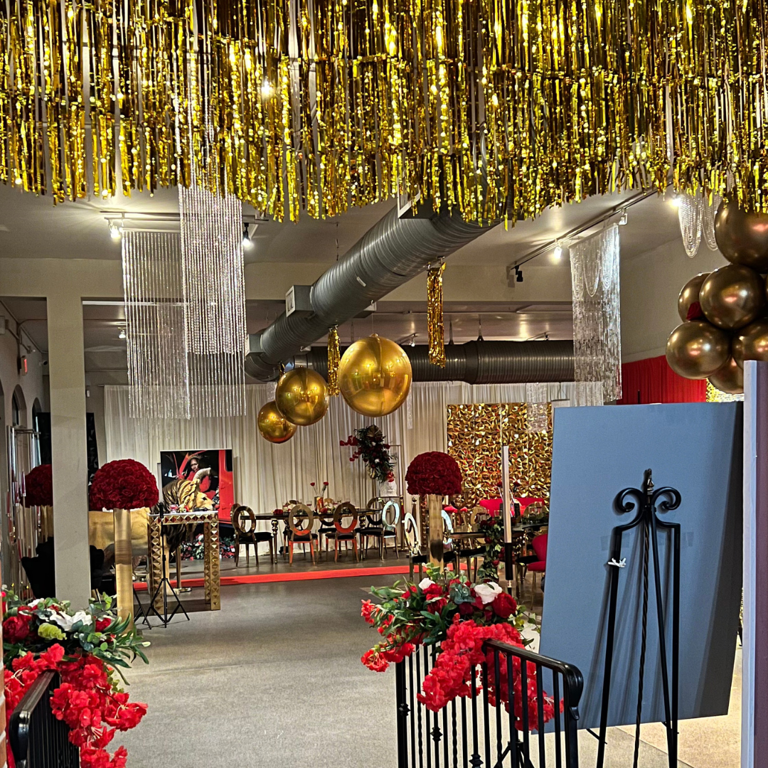 A decorated event space with gold and red decorations, including gold balloons, red flowers, and gold streamers hanging from the ceiling.