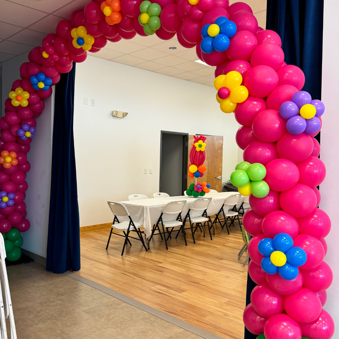 Colorful balloon arch and decorations inside a decorated room, possibly for a celebration or party.
