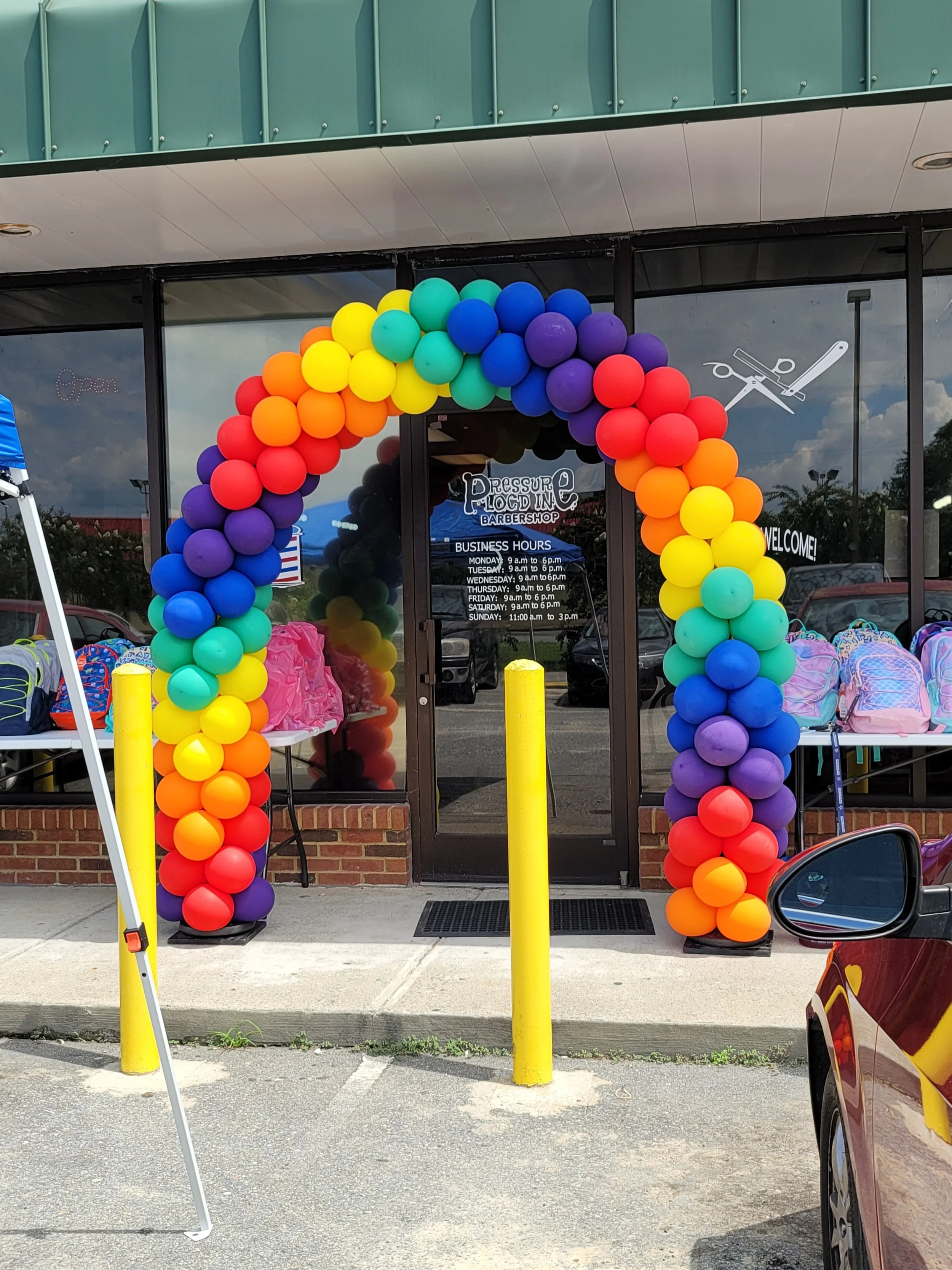 Colorful balloon arch in rainbow pattern outside a barbershop entrance.