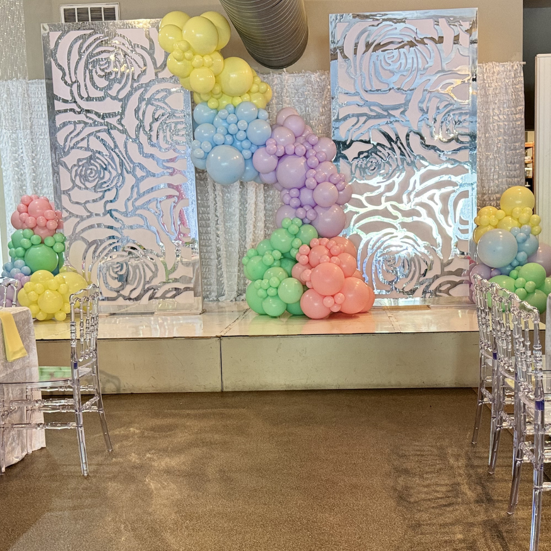 Decorative backdrop with floral cutouts and pastel-colored balloons for a celebration or party.