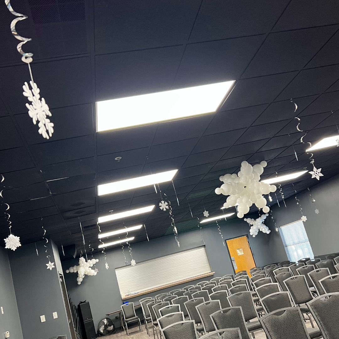 Empty event room decorated with white snowflake and balloon ornaments hanging from the black ceiling.