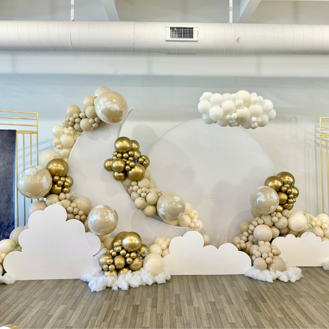 Cloud-themed balloon decoration with large white, gold, and pearl balloons arranged on a white backdrop with cloud cutouts, creating a whimsical sky scene.