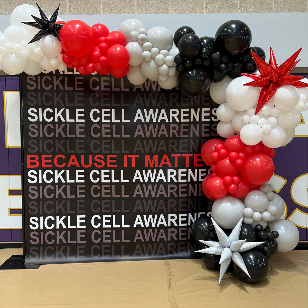 Balloon display with red, white, and black balloons decorated around a Sickle Cell Awareness board with the message, 'Because it matters' in red text.