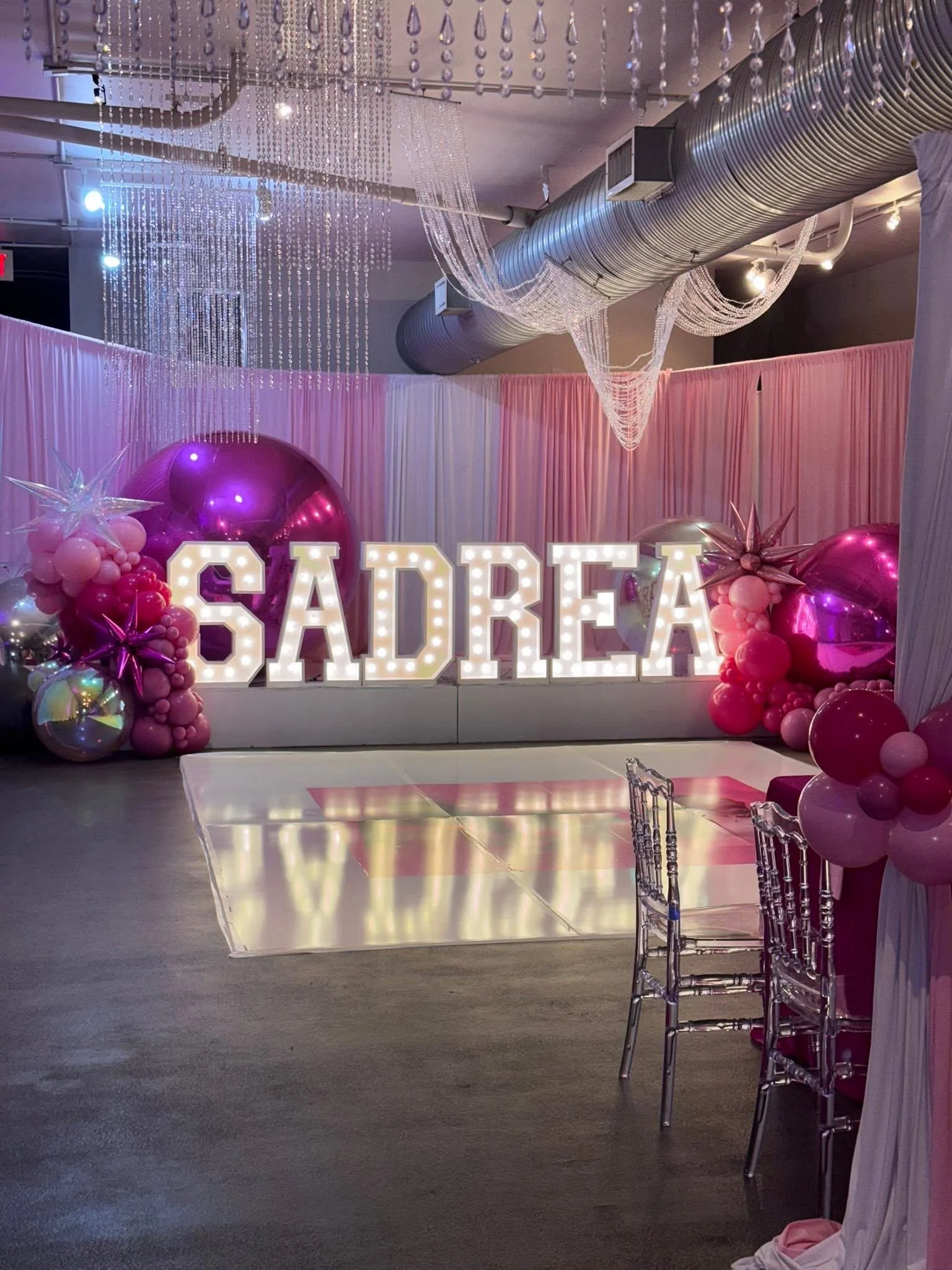Decorated event space with pink and purple balloons, backdrop, and illuminated signs spelling 'SADREA'