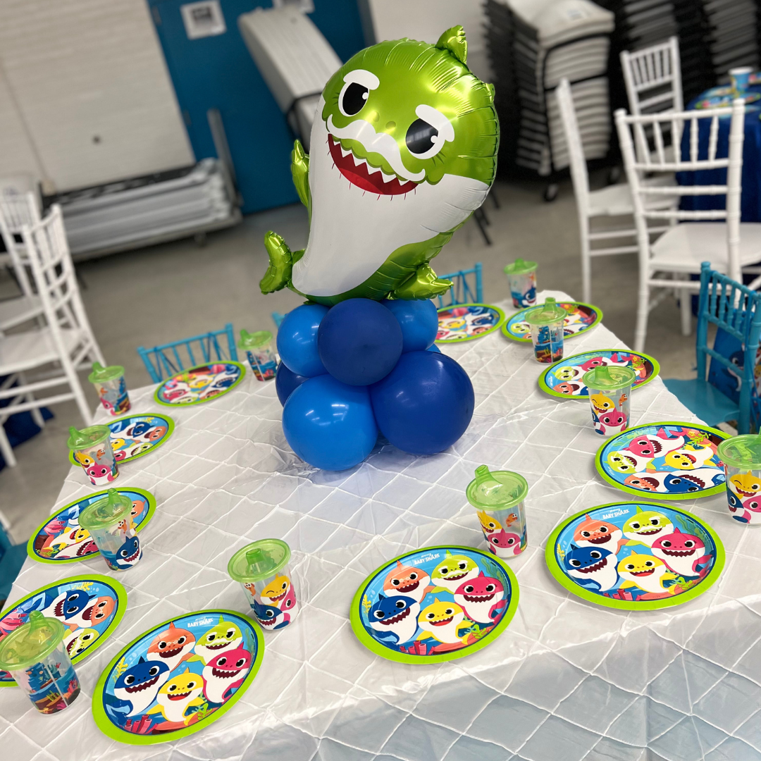 Party table decorated with a Shark Tales theme, featuring a shark foil balloon, colorful plates with sharks, and matching cups, set for a child's birthday celebration.