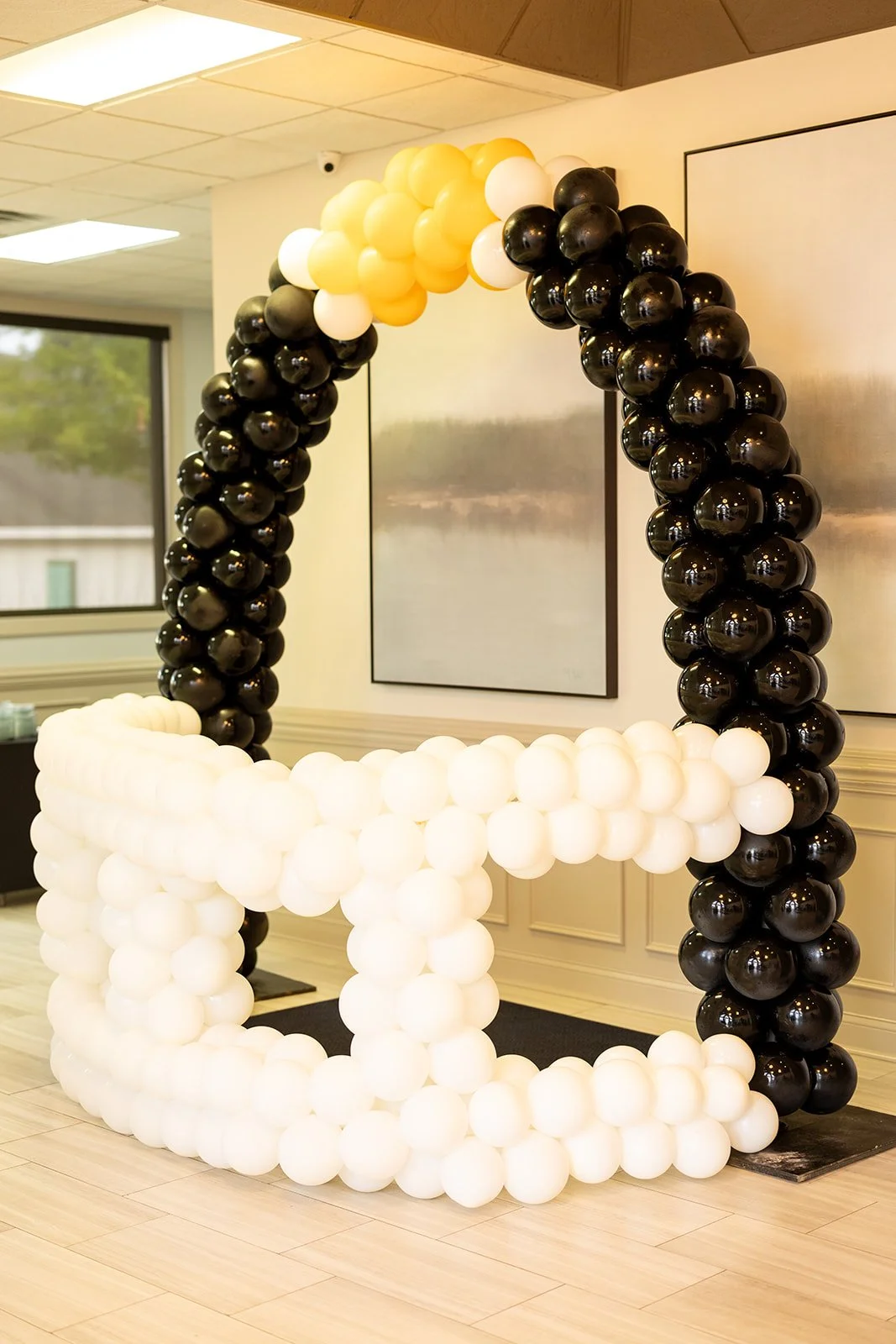Balloon arch and letter sculpture at an indoor event, featuring black and white balloons.