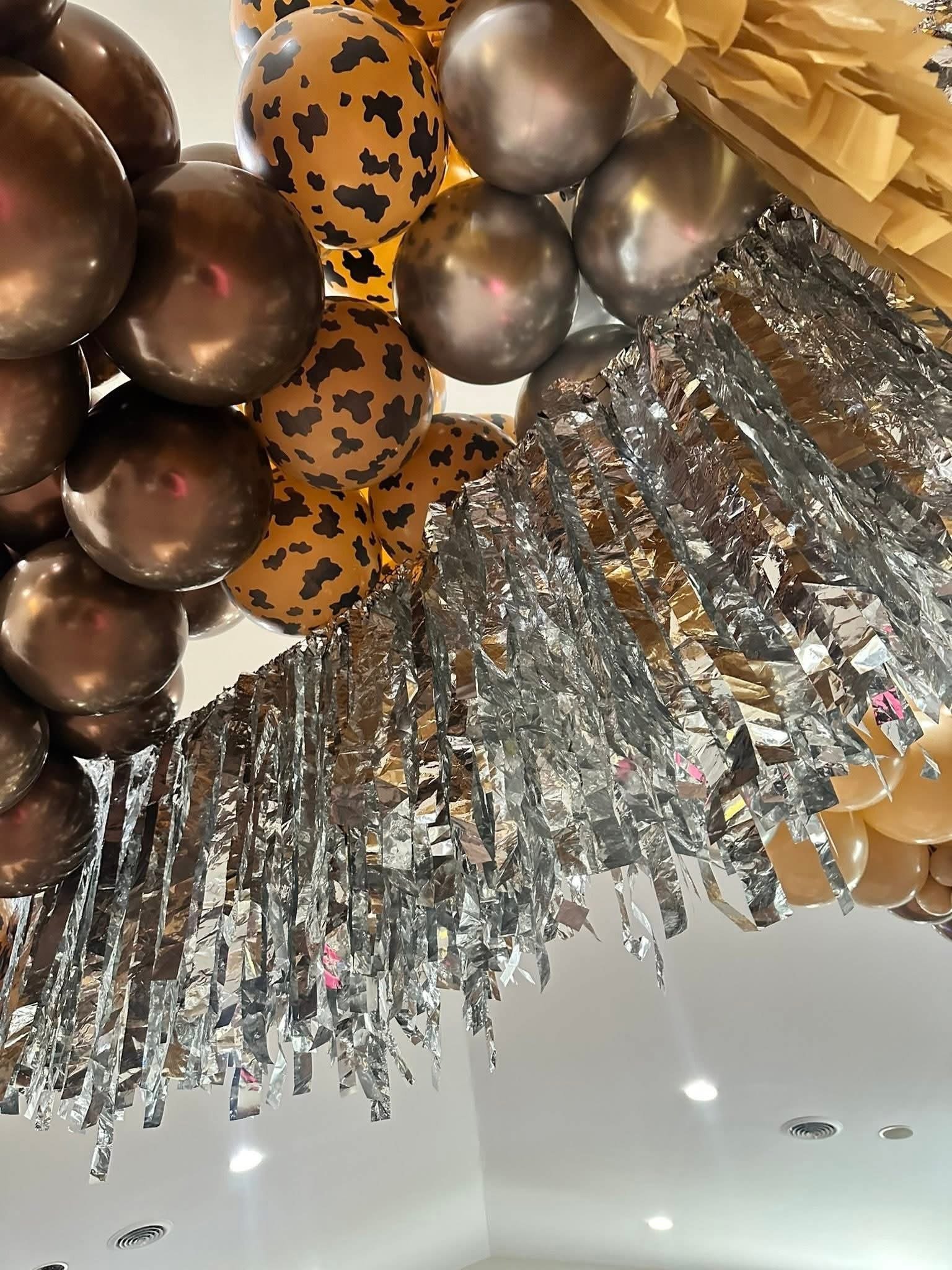 Close-up view of gold, silver, and leopard-print balloons hanging from ceiling with foil fringe decorations underneath.
