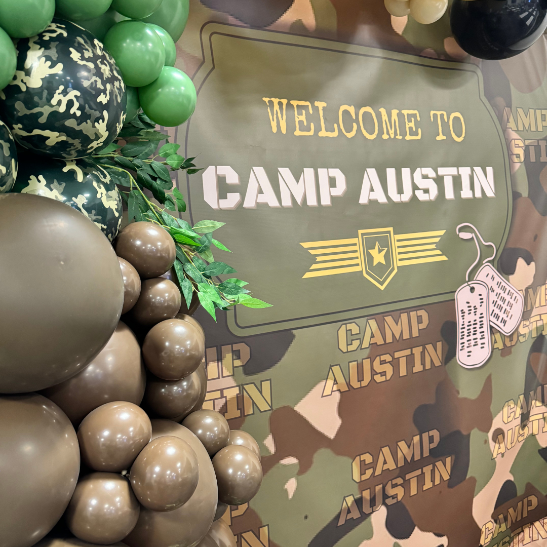 Decorative balloons arranged next to a sign that reads 'Welcome to Camp Austin' on a camouflage-patterned background.