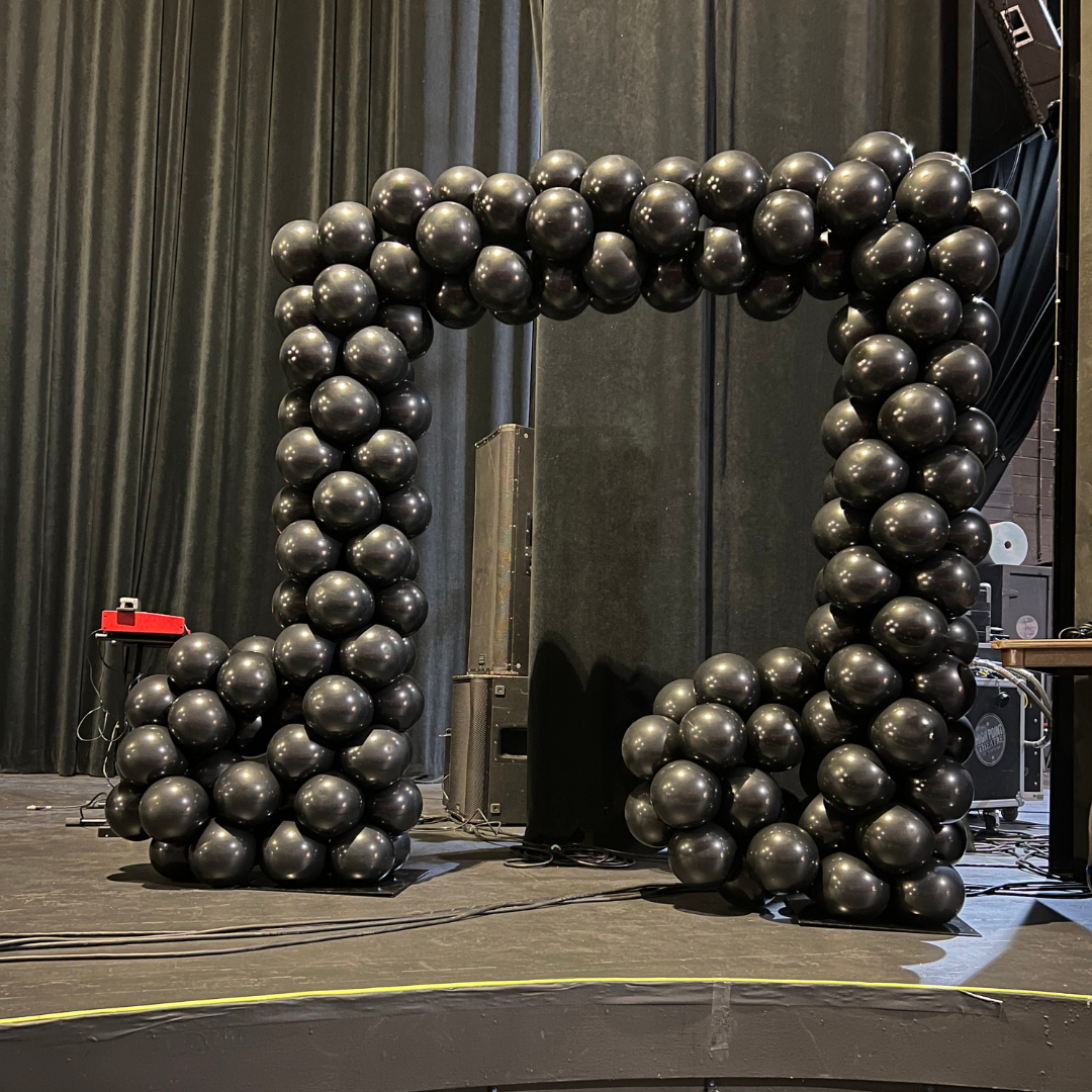 Stage decorated with black balloon arch and columns, with black curtains in the background.