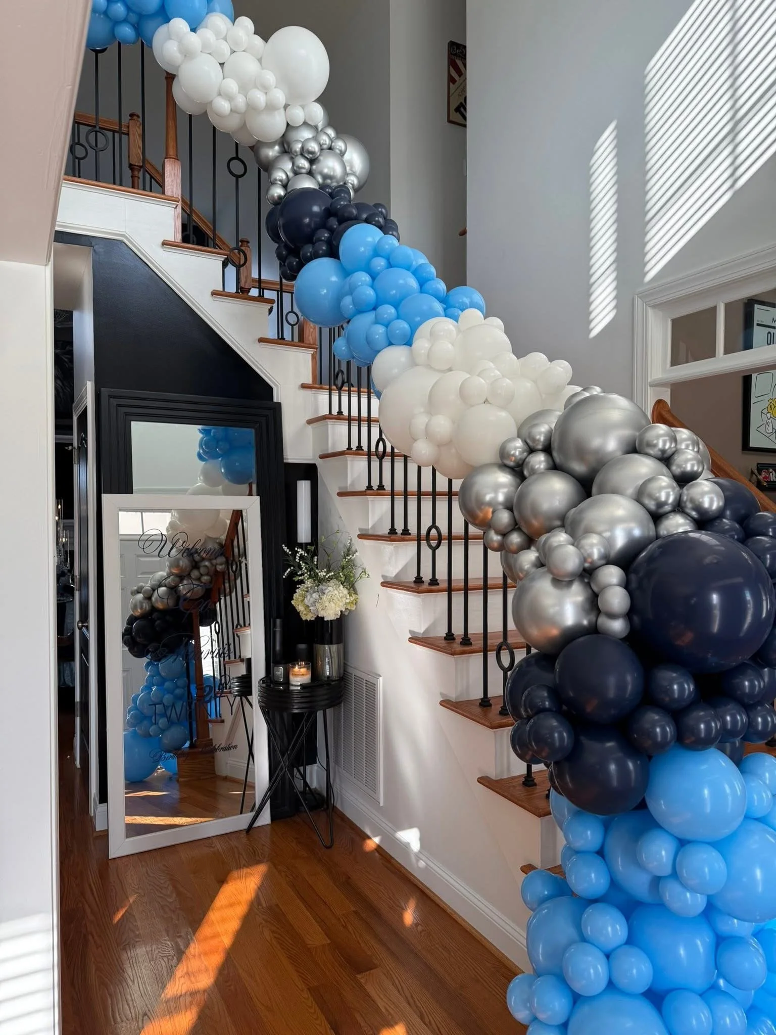 Decorative balloon arch with white, black, blue, and silver balloons running along the staircase handrail in a brightly lit interior.