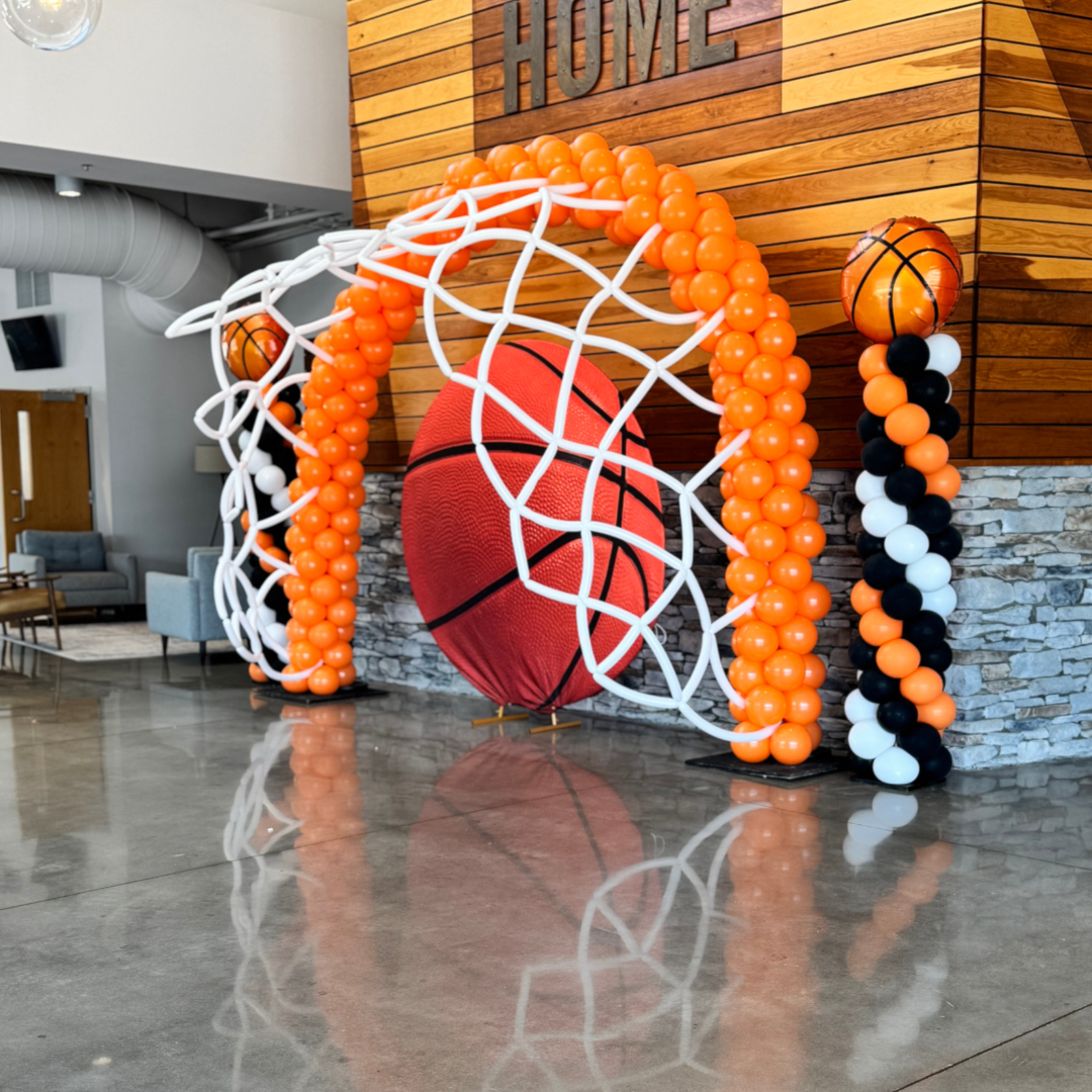 Basketball-themed balloon decoration with an orange arch and columns, featuring basketball ball balloons and a mesh basketball.