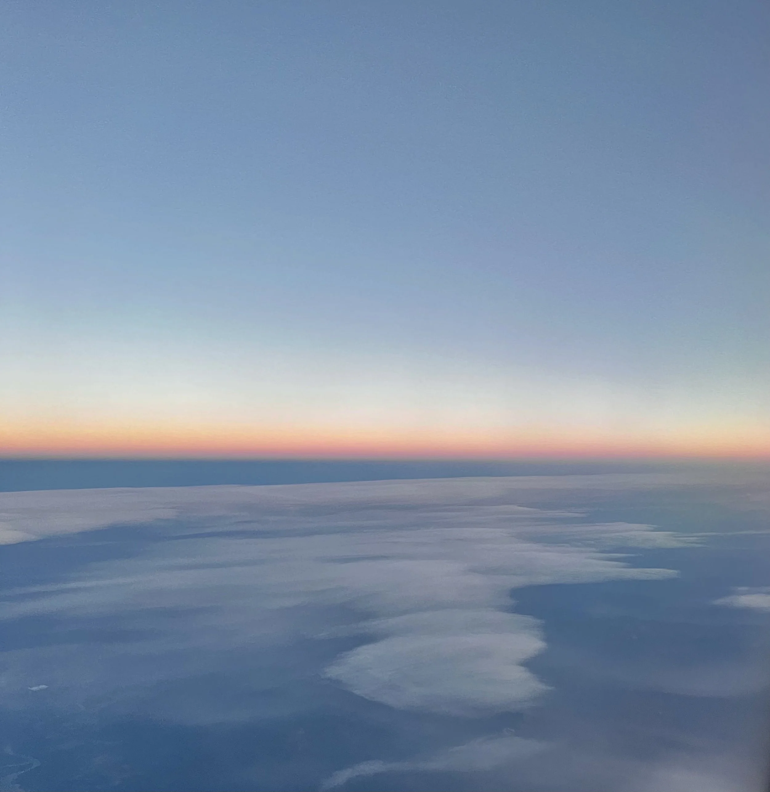 Aerial view of the sky and clouds at sunset, with a subtle gradient of colors from blue to pink and orange near the horizon.