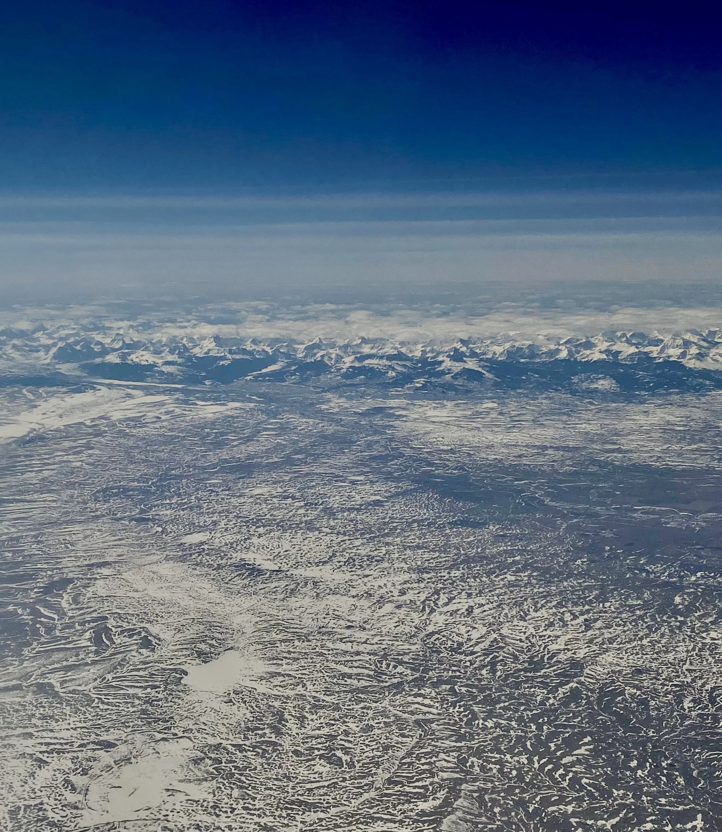 Aerial view of snow-covered mountain range under a clear blue sky.