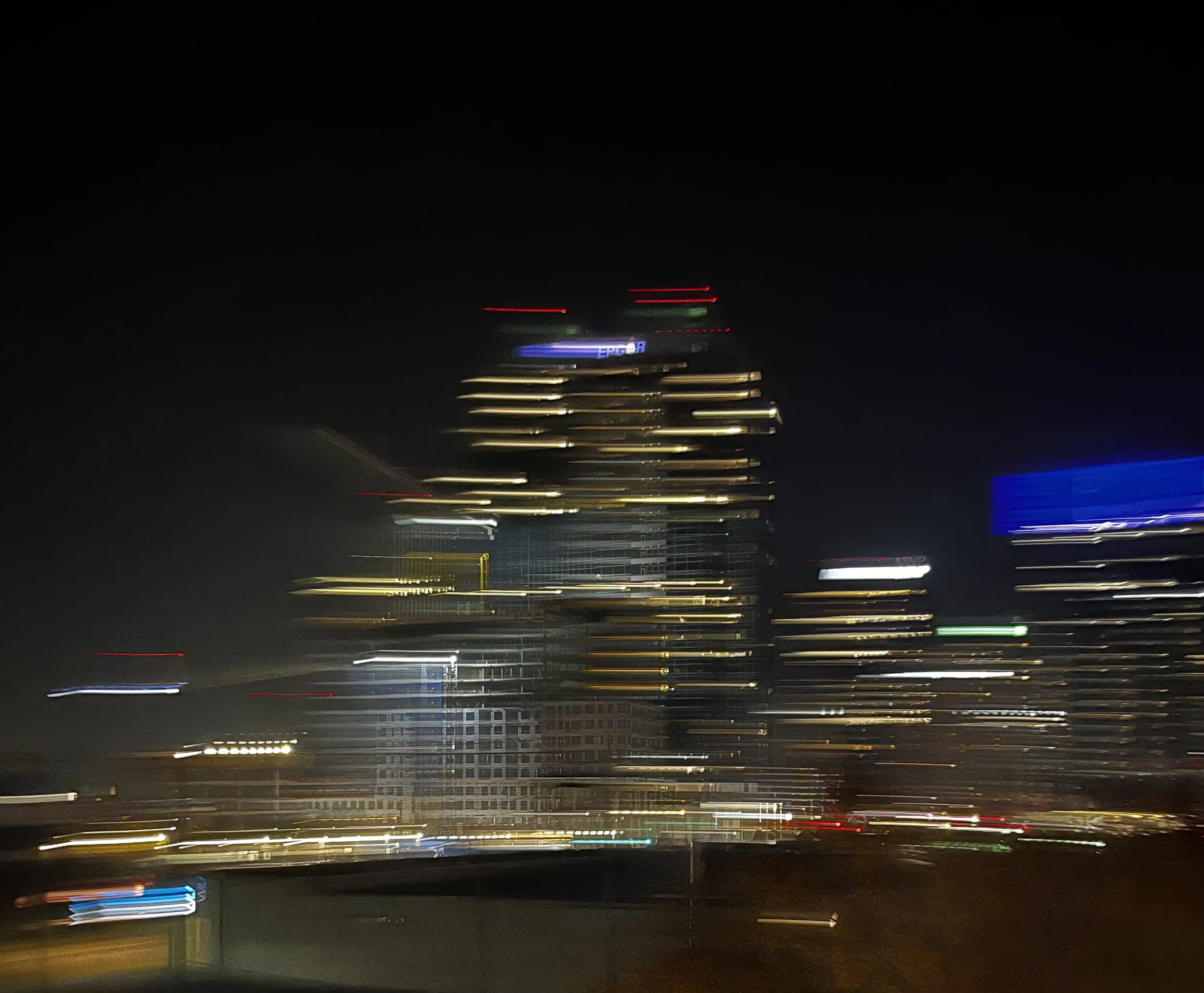 Night view of a city with tall buildings and city lights, with motion blur effects.