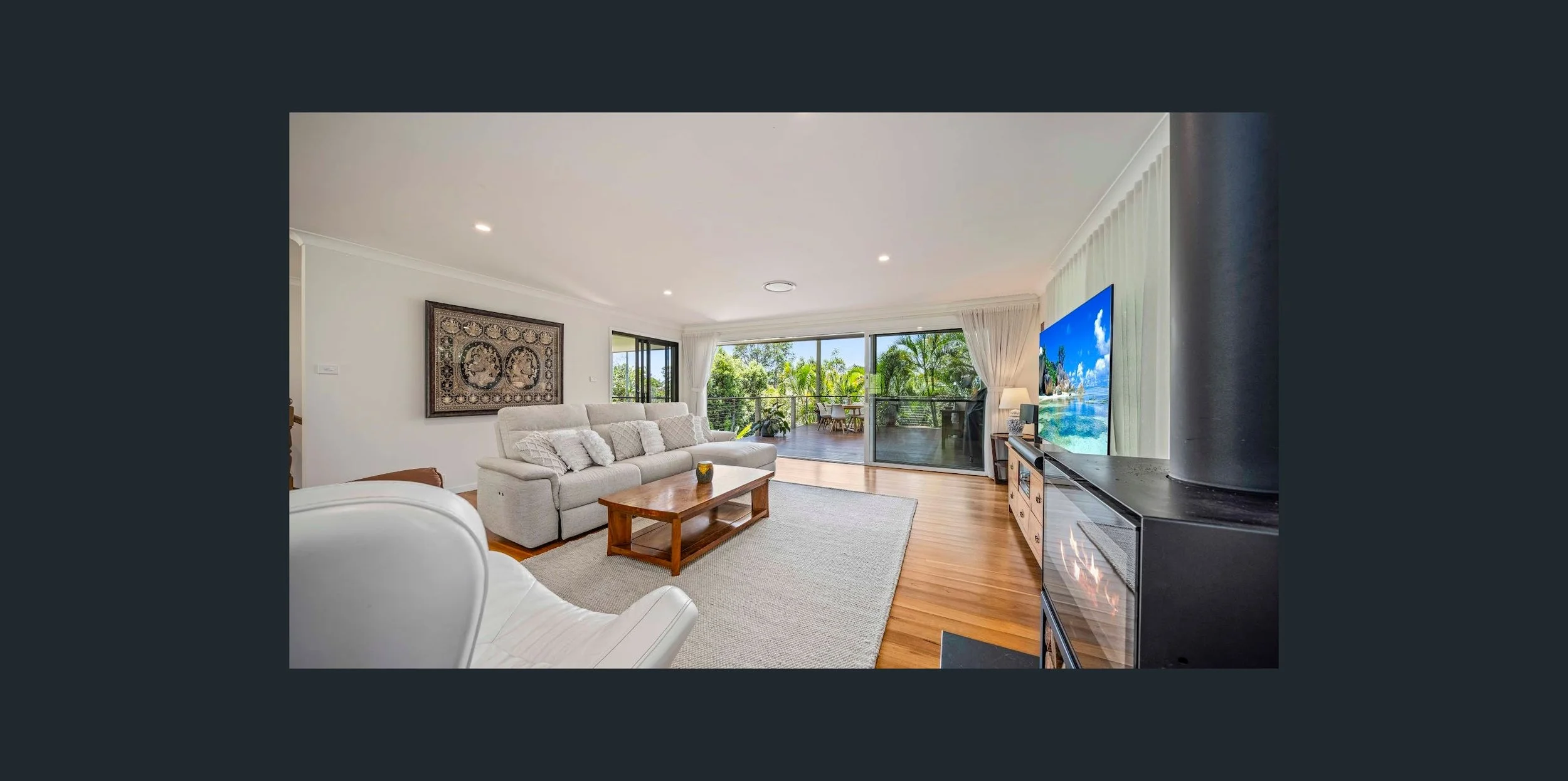 Living room with white sofa, wooden coffee table, and sliding glass door leading to outdoor balcony with greenery.