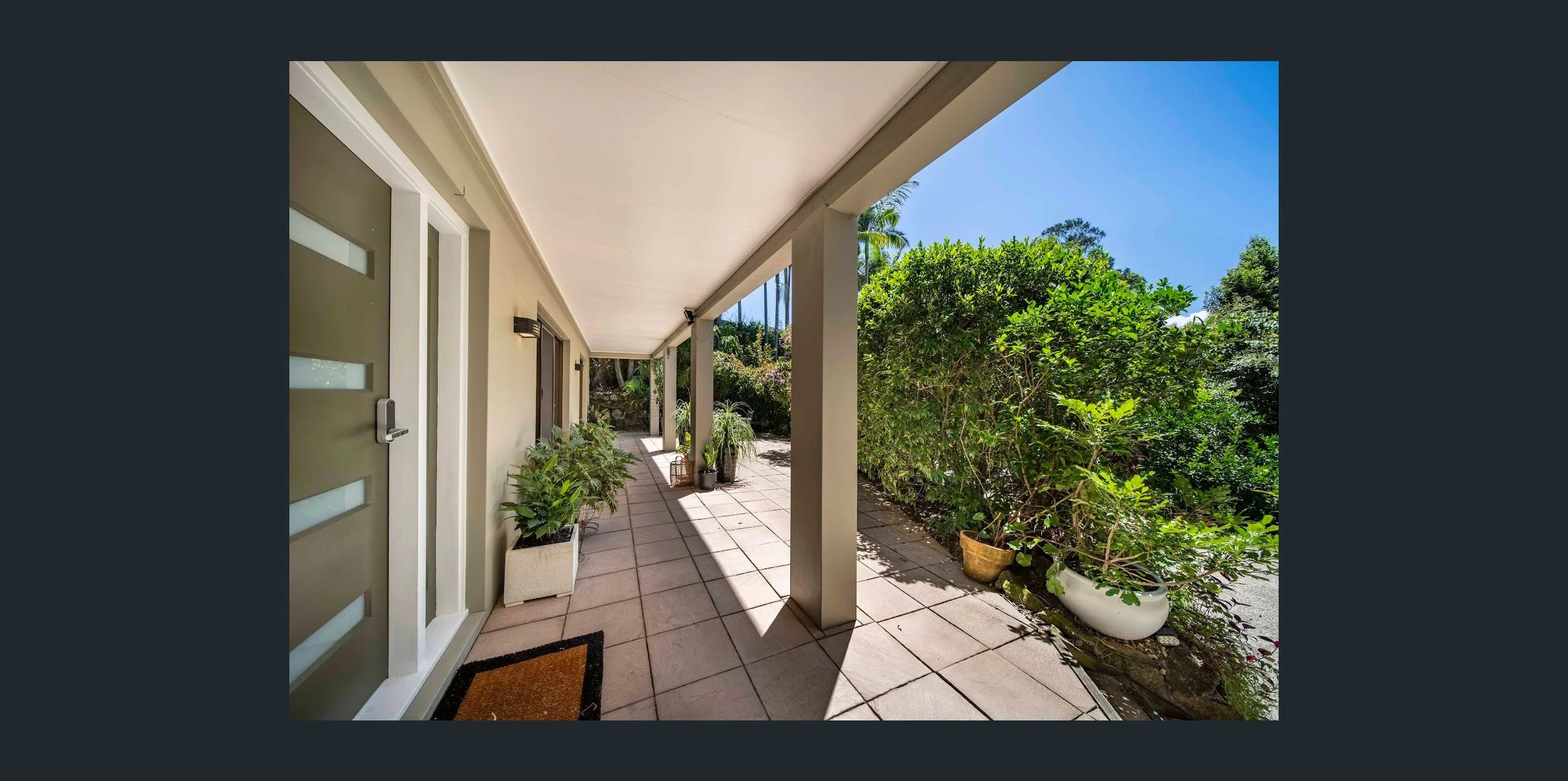 Outdoor patio with potted plants, tiled flooring, and lush greenery on a sunny day.