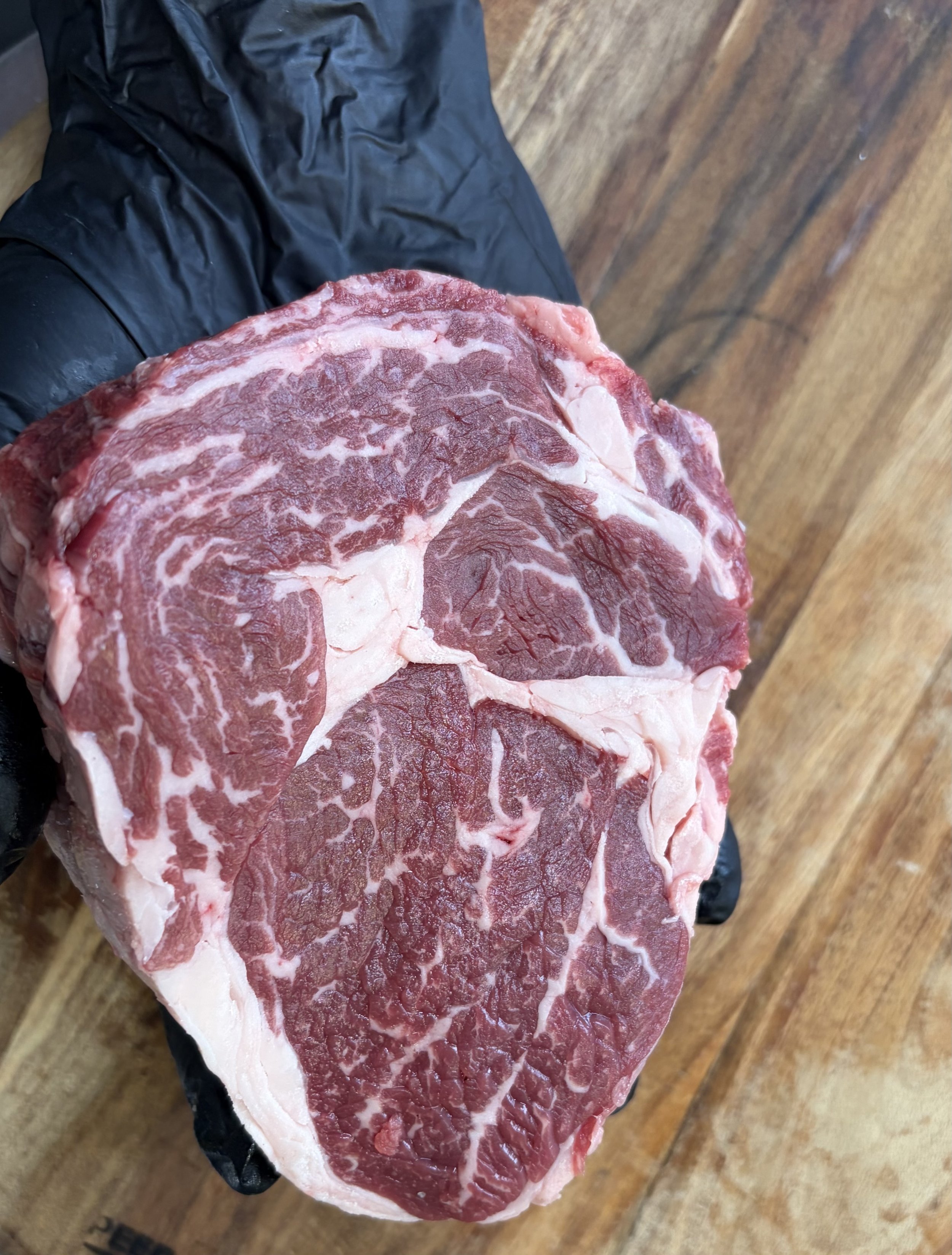 Close-up of a large piece of raw marbled scotch fillet, held by a gloved hand.