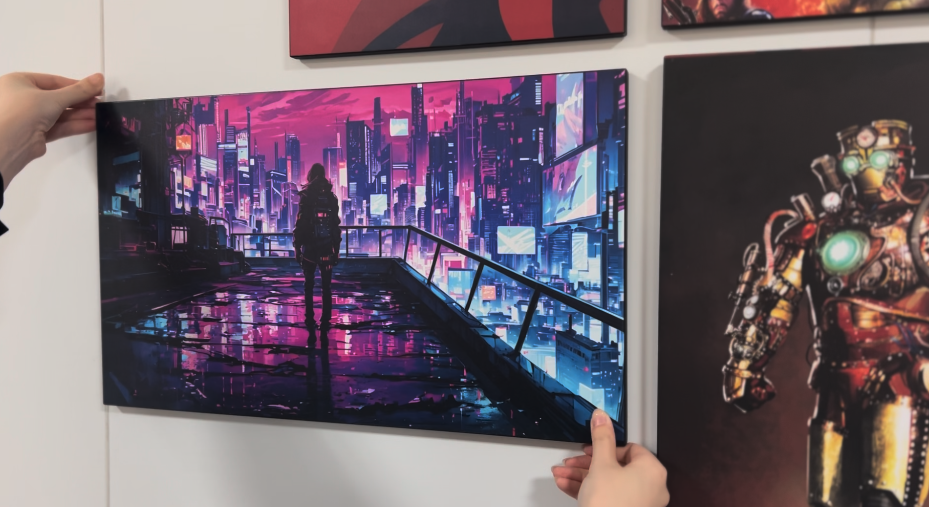 A person is holding a large digital art print of a futuristic cityscape with neon lights and a person walking on a rooftop, with another poster partially visible in the background.