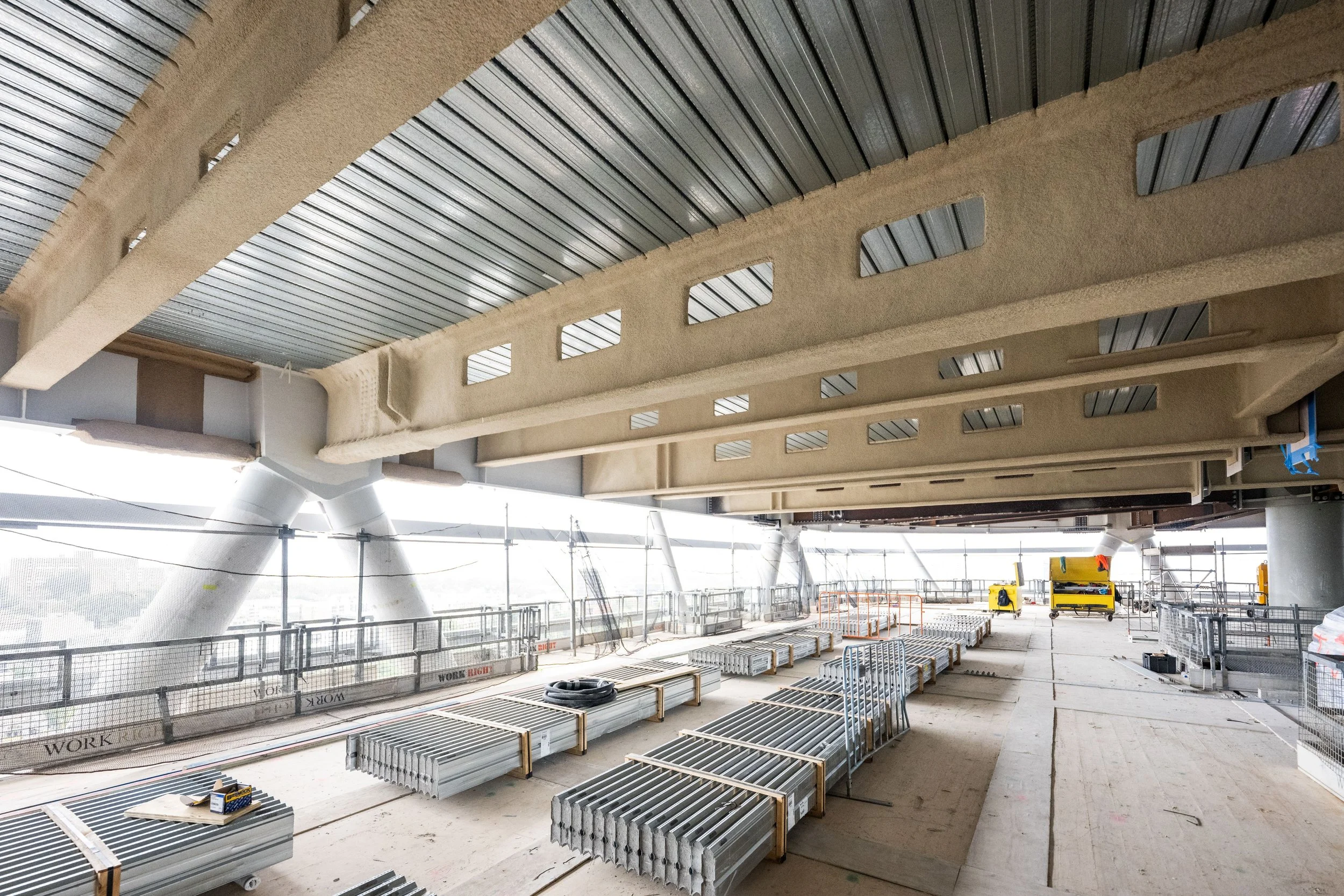 Construction site with metal framework, scaffolding, and equipment inside a large building under construction.
