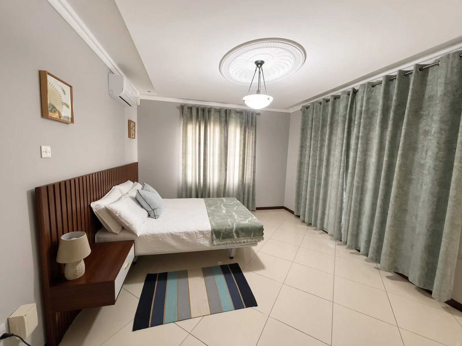 Furnished bedroom with fitted wooden headboard, aircon and green curtains in the 5-bedroom house for rent, Phakalane. Nestgeeks.