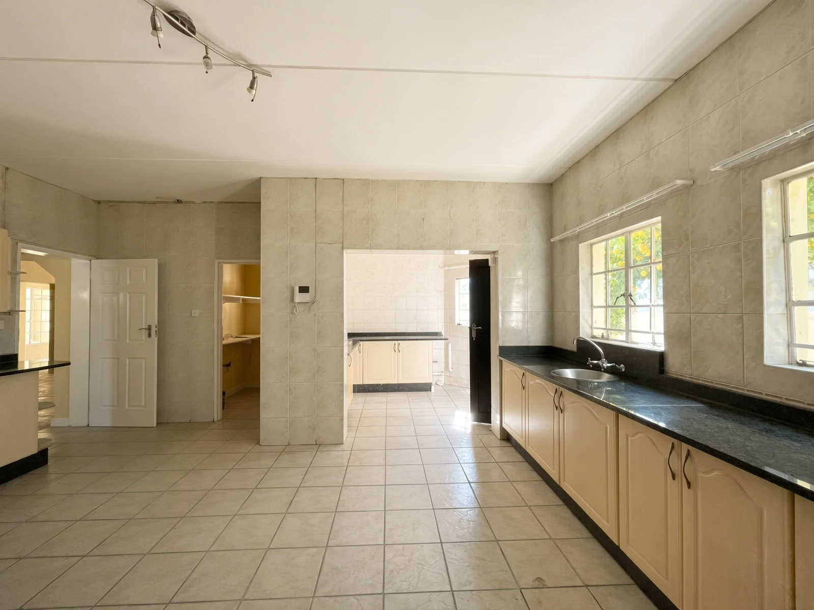 Open kitchen with cream cabinets, double sink and scullery beyond in a 5-bedroom rental in Block 9 Gaborone