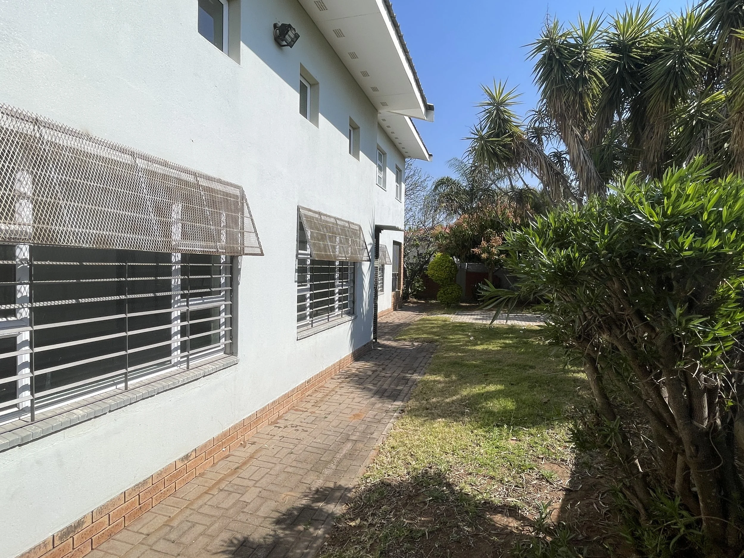 Exterior of the 4-bedroom house with security window bars, paved walkway and garden in a gated estate, Phakalane. Nestgeeks.