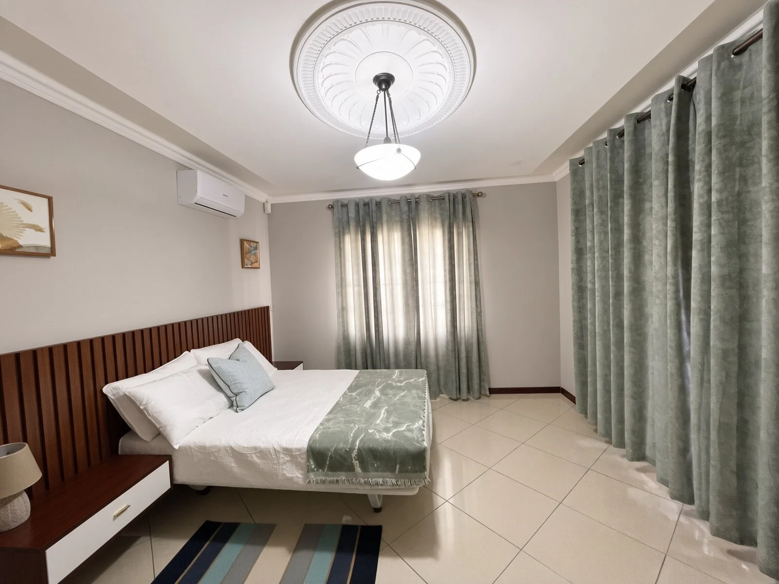 Air-conditioned bedroom with wooden slat headboard and sage green curtains in the fully furnished 5-bedroom Phakalane rental. Nestgeeks.