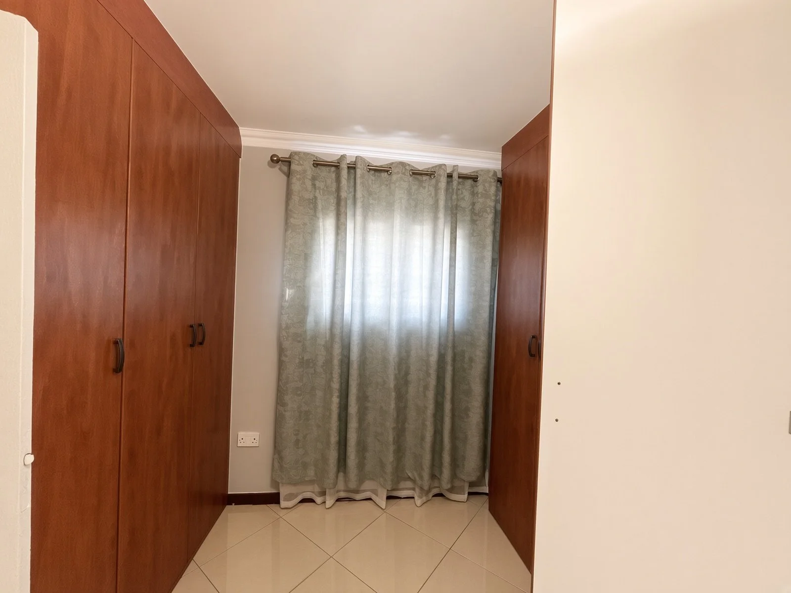 Fitted wooden wardrobes and window with curtains in one of the bedrooms of the fully furnished 5-bedroom house for rent in Phakalane. Nestgeeks.