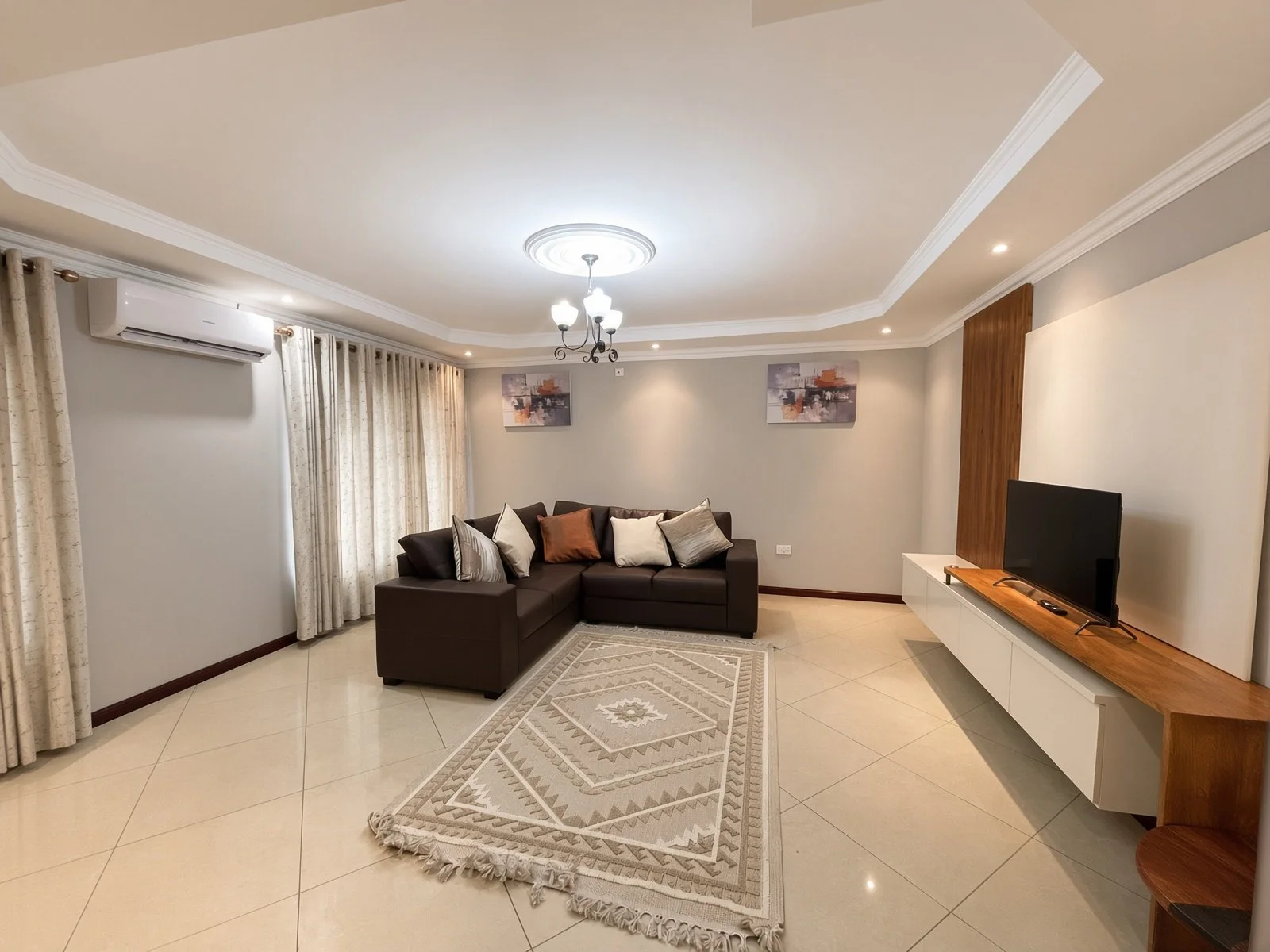 Air-conditioned lounge with brown leather L-shaped sofa, feature rug and TV unit in the fully furnished 5-bedroom home for rent, Phakalane. Nestgeeks.