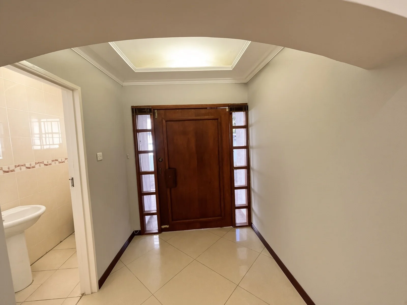 Wooden front door with glass sidelights and guest toilet basin at the entrance of the fully furnished 5-bedroom house for rent in Phakalane. Nestgeeks.