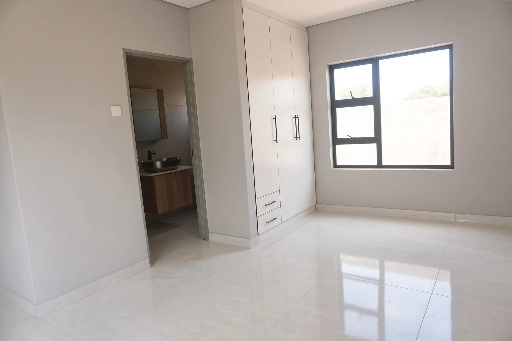 Spacious bedroom with floor-to-ceiling white fitted wardrobes, large window and ensuite bathroom visible in this 3-bedroom house for rent in a gated estate, Gaborone North. Nestgeeks property.
