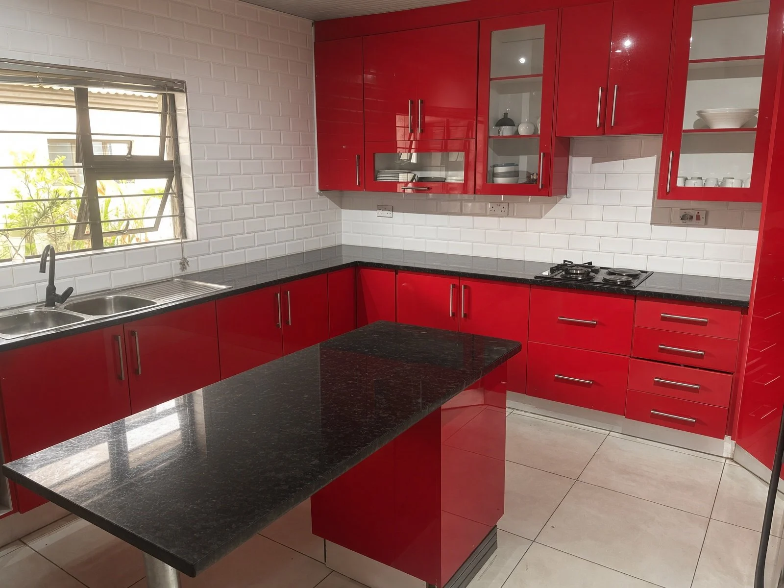 Open red kitchen with granite island, double sink and white subway tiles in a house for sale in Gaborone North