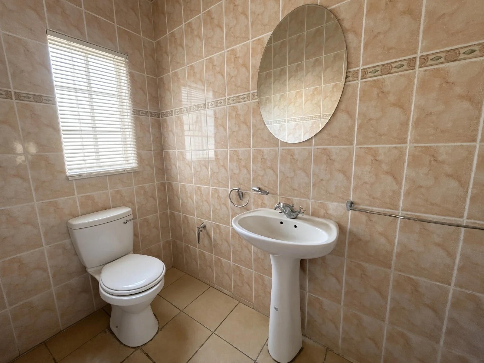 Guest toilet with pedestal basin, oval mirror and window blinds in a family house for rent in Block 9 Gaborone