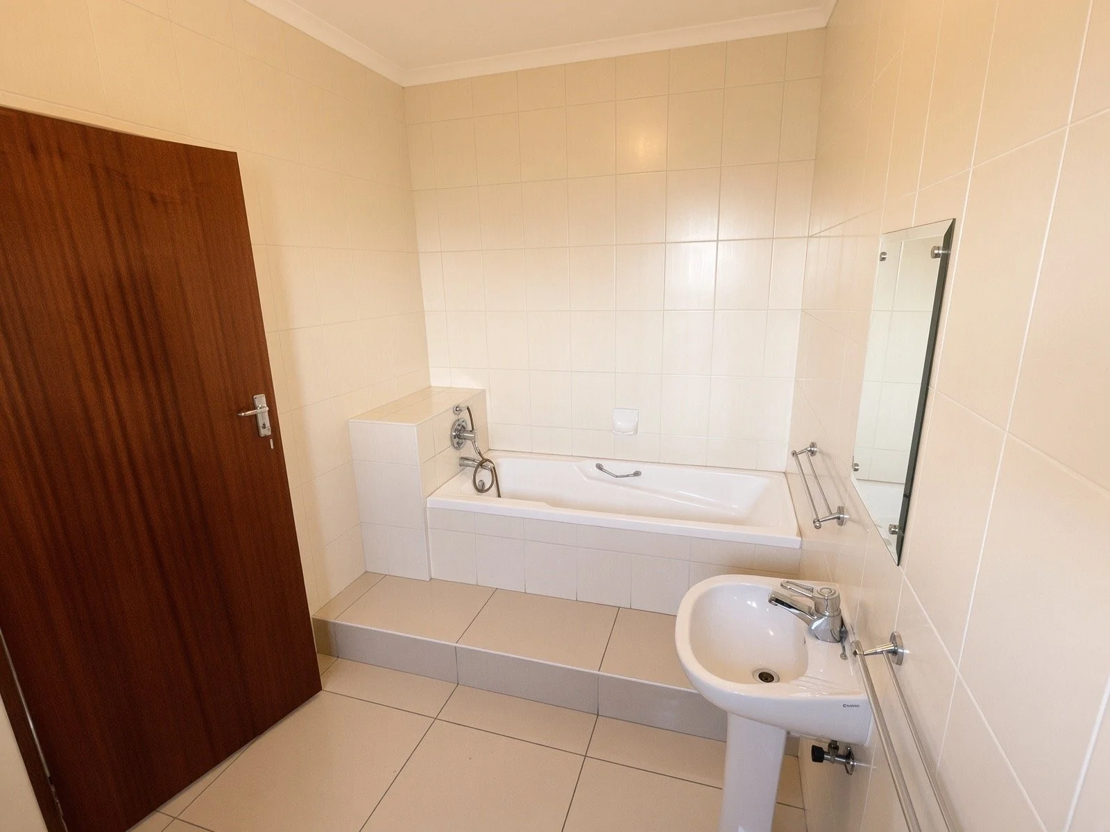 Bathroom with bathtub, pedestal basin and beige tiling in the 4-bedroom rental home, Phakalane gated estate. Nestgeeks.
