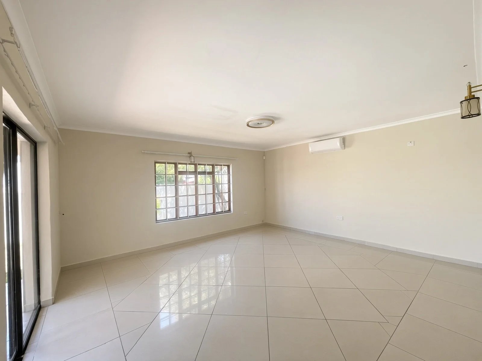 Bright tiled lounge with air conditioning and barred window in a family house for rent in Phakalane
